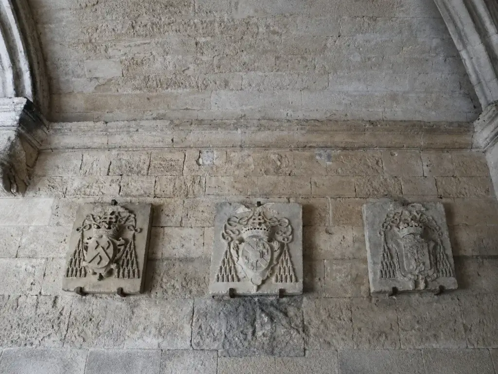 Trois plaques armoriées en pierre présentées contre un mur du cloître Saint-Trophime à Arles.